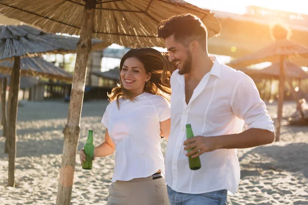 Pareja feliz sonriendo y bebiendo cerveza en la playa — Foto de Stock