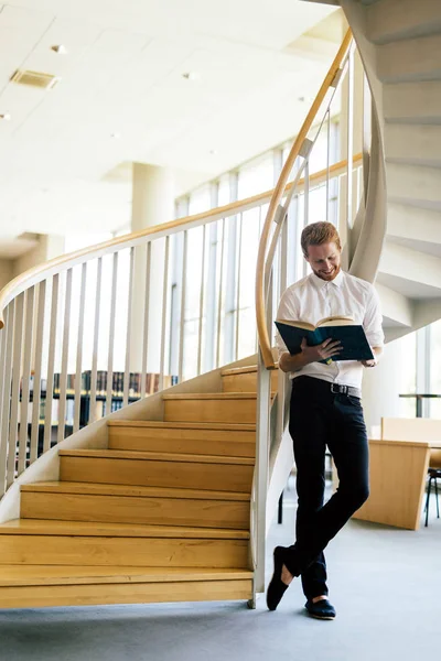 Bonito tipo inteligente lendo um livro em uma biblioteca — Fotografia de Stock