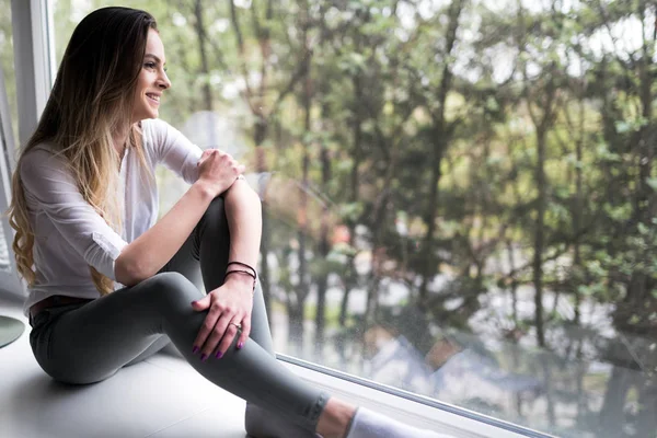 Beautiful woman sitting on window ledge — Stock Photo, Image