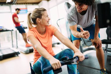 Genç ve güzel bir kadın spor salonunda antrenörle egzersiz yapıyor.