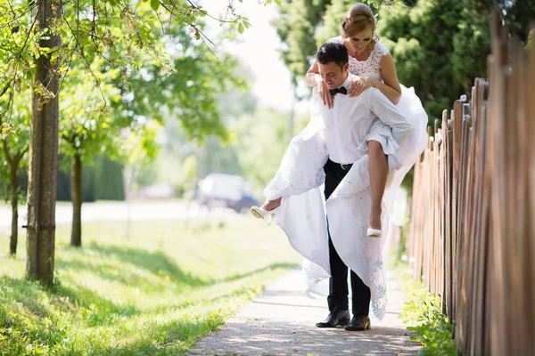 Brudgummen bär bruden piggyback — Stockfoto