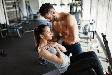 Genç kadının spor salonunda kişisel antrenör ile abs için egzersizler yapması