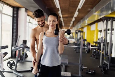 Genç seksi kadının pazı eğitmen ile spor salonunda egzersiz yapması