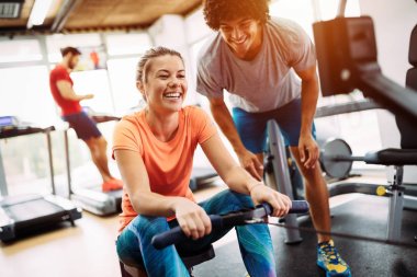 Genç ve güzel bir kadın spor salonunda antrenörle egzersiz yapıyor.
