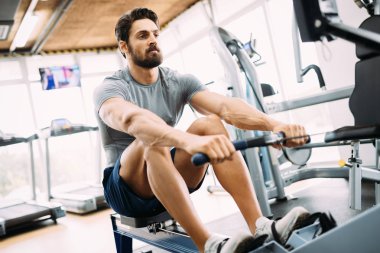 Yakışıklı delikanlı kürek makine üzerinde spor salonunda egzersizleri yapıyor