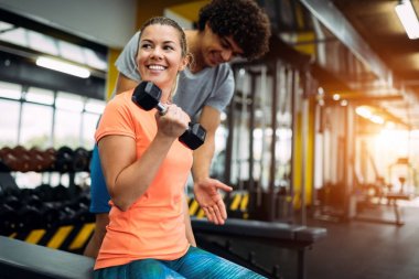 Genç ve güzel bir kadın spor salonunda antrenörle egzersiz yapıyor.