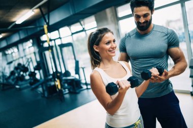 Genç ve güzel bir kadın spor salonunda antrenörle egzersiz yapıyor.
