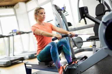Spor salonunda kürek makine üzerinde çalışan genç sarışın kadın