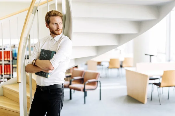 Schöner intelligenter Kerl liest ein Buch in einer Bibliothek — Stockfoto