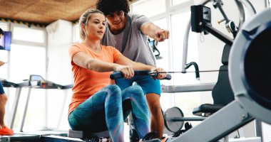 Genç ve güzel bir kadın spor salonunda antrenörle egzersiz yapıyor.