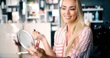 Genç ve güzel bir kadın aynanın yanında makyaj yapıyor.