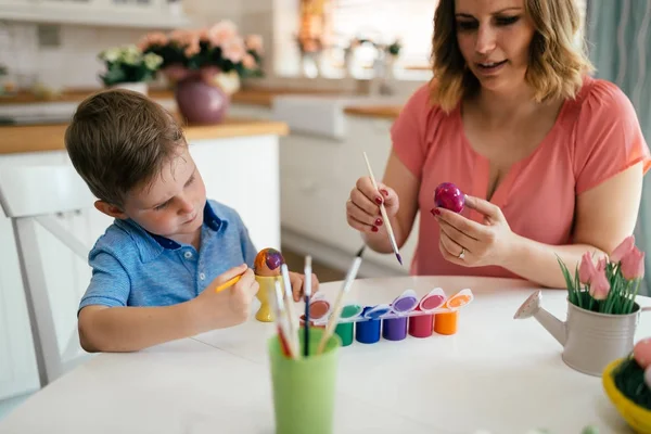 Jovem mãe e seu filho se divertindo enquanto pinta ovos para a Páscoa — Fotografia de Stock