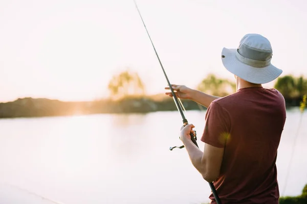 Joven pescando en el lago al atardecer disfrutando hobby —  Fotos de Stock