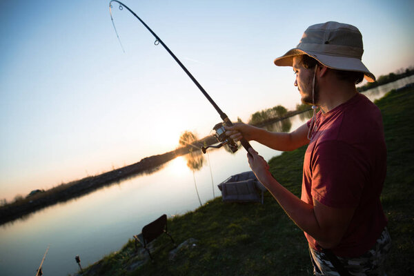 Young man fishing at pond and enjoying hobby