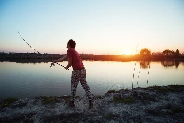 Joven pescando en un lago al atardecer y disfrutando de hobby —  Fotos de Stock