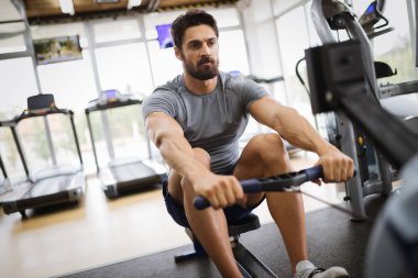 Yakışıklı delikanlı kürek makine üzerinde spor salonunda egzersizleri yapıyor