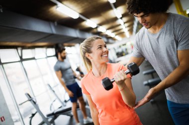 Genç ve güzel bir kadın spor salonunda antrenörle egzersiz yapıyor.