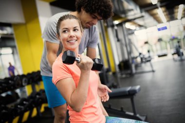Güzel bir kadın spor salonunda kişisel antrenörüyle biceps egzersizleri yapıyor.