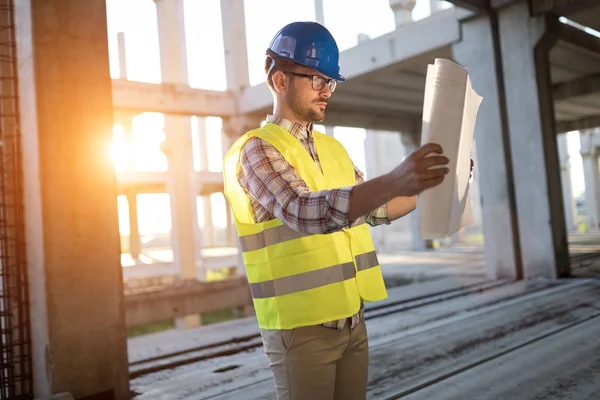 Portrait of male site contractor engineer with hard hat holding blue print paper at construction site,