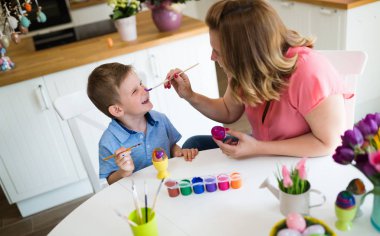 Mutlu genç anne ve oğlu Paskalya yumurta boyama bir masada oturuyor