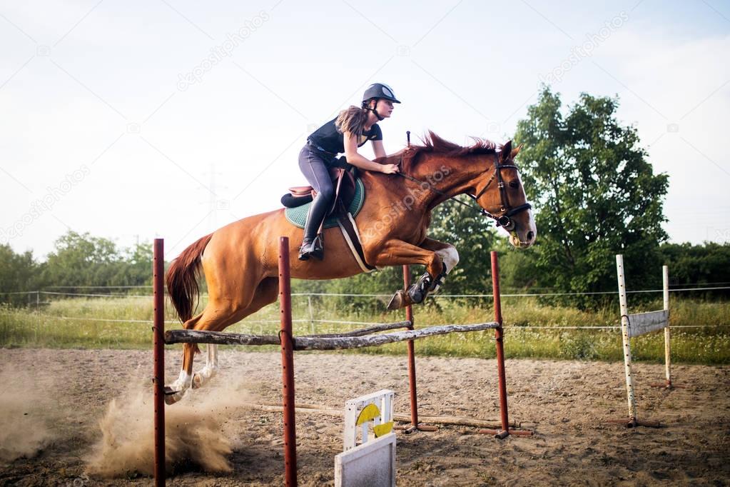 Young female jockey on her horse leaping over hurdle