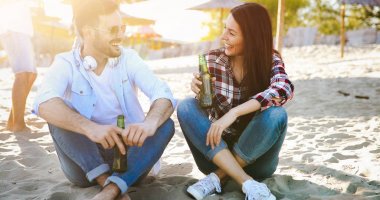 Mutlu çift gülümseyen ve sahilde bira içmek