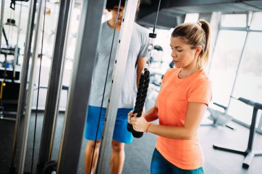 Genç ve güzel bir kadın spor salonunda antrenörle egzersiz yapıyor.