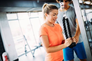 Genç ve güzel bir kadın spor salonunda antrenörle egzersiz yapıyor.