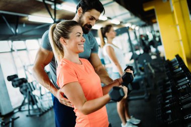 Genç ve güzel bir kadın spor salonunda antrenörle egzersiz yapıyor.