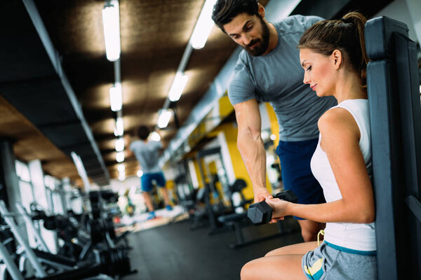 Young beautiful woman doing exercises with personal trainer in gym