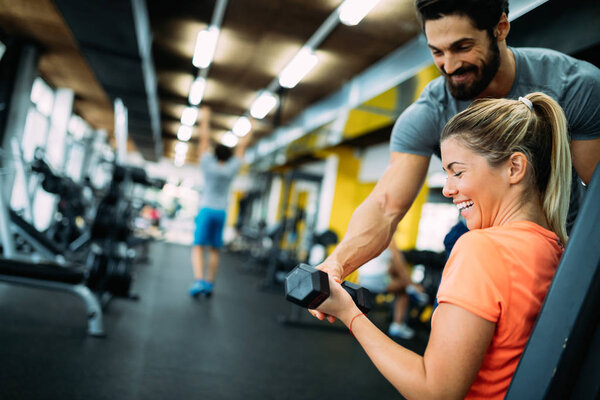 Young beautiful woman doing exercises with personal trainer in gym