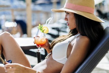 Onun kokteyl içme ve bir şapka ve beyaz bir bikini giyen süre güneşlenme çarpıcı güzelliği