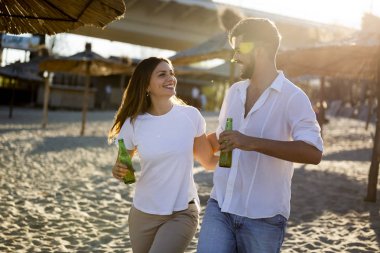 Kumsalda gülümseyen ve bira içen mutlu genç çift