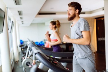 Kardiyo egzersiz yaparken spor salonunda koşu bandı üzerinde çalışan insanlar