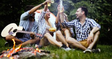 Mutlu arkadaşlar müzik çalıyor ve doğada şenlik ateşinin keyfini çıkarıyorlar.