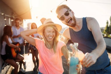 Bir grup mutlu genç arkadaş çatıda parti veriyor.