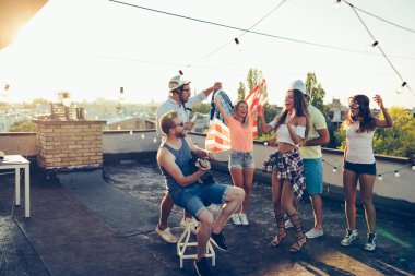 Bir grup mutlu genç arkadaş çatıda parti veriyor.