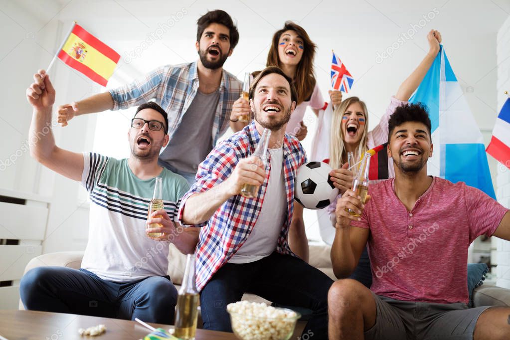 Cheerful and happy group of friends watching football game on tv.