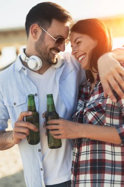Kumsalda gülümseyen ve bira içen mutlu genç çift