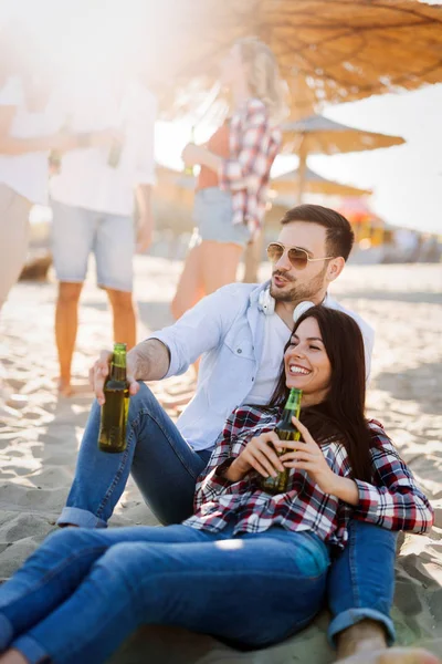 幸せな若いカップル笑顔とビーチでビールを飲む — ストック写真