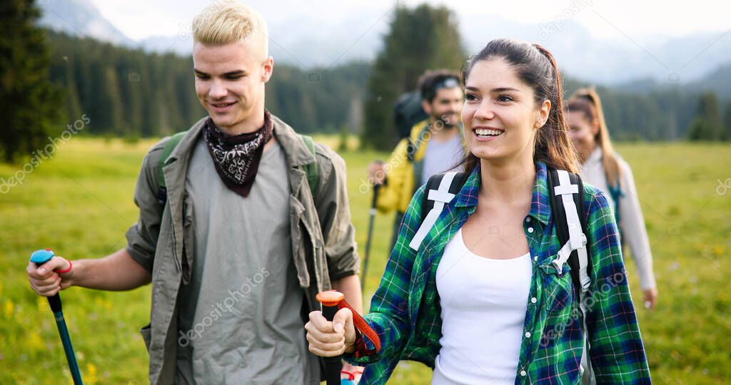 Young gorup of friends climbing up hill, with backpacks and climbing stick