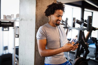 Spor salonunda egzersiz yaparken telefonu kullanan formda bir genç..