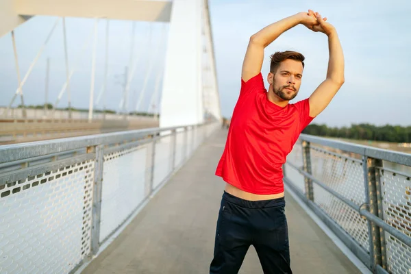 Hermoso corredor masculino estiramiento antes del entrenamiento, hombre en forma haciendo ejercicios al aire libre — Foto de Stock
