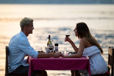 Genç çift deniz kıyısında romantik bir akşam yemeği yiyor.