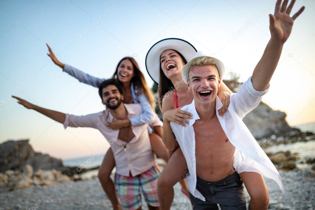 Group of happy friends having fun on the beach under sunset on vacation