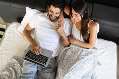 Yatak odasında dizüstü bilgisayar kullanan mutlu genç çift.