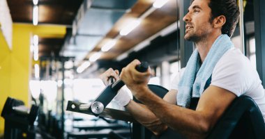 Spor salonunda egzersiz yapan kaslı, formda bir adam. İki kollu halterle egzersiz yapıyor.
