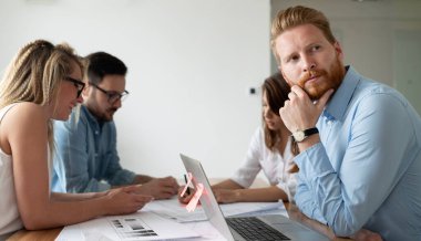 İş arkadaşlarıyla birlikte ofis masasında otururken çalışan ve iletişim kuran bir grup genç iş adamı