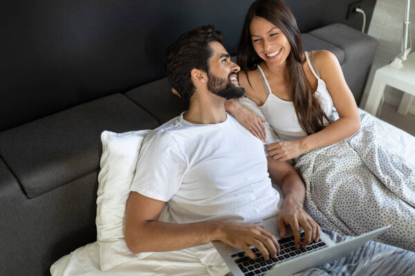 Happy young couple using laptop on bed at bedroom