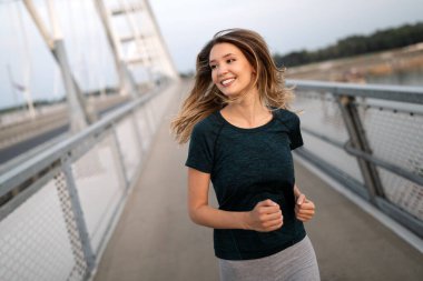 Güzel formda mutlu koşucu kadın köprüden geçiyor.